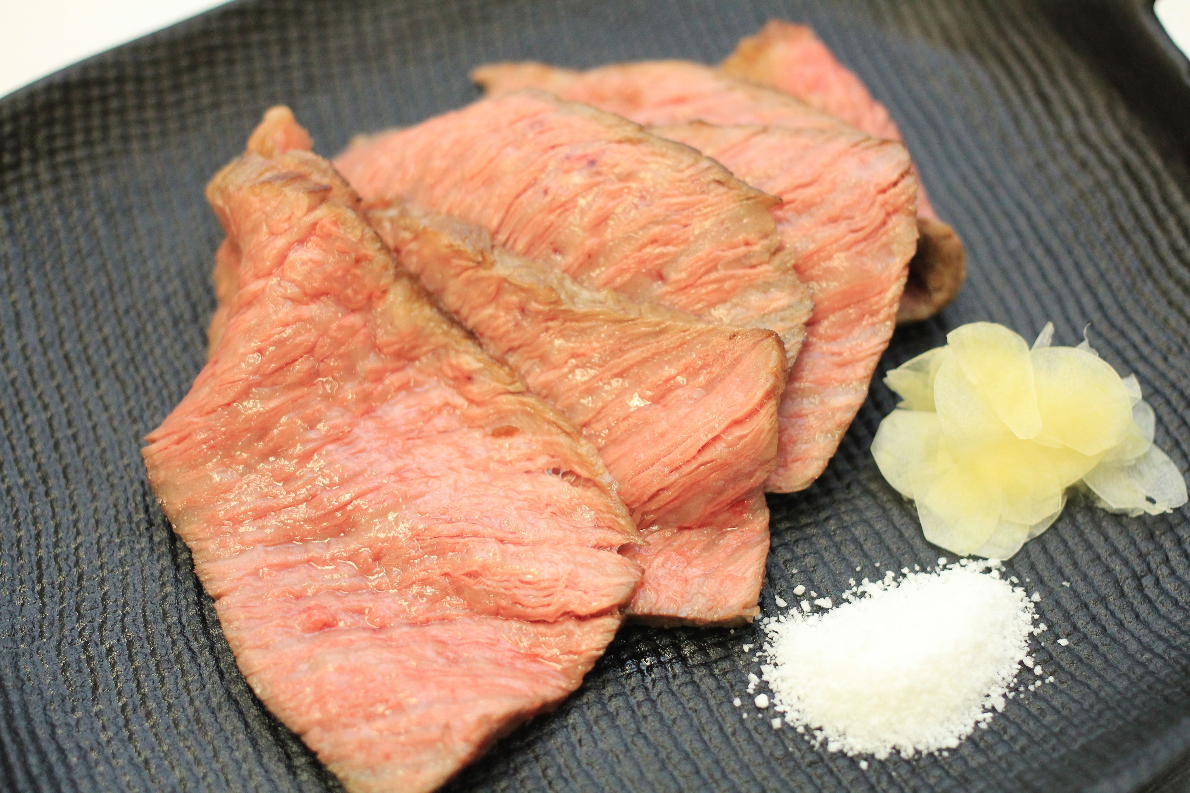 Slices of pink meat on a textured plate with a small pile of white powder and a yellow flower.