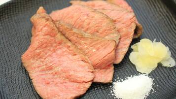 Slices of pink meat on a textured plate with a small pile of white powder and a yellow flower.