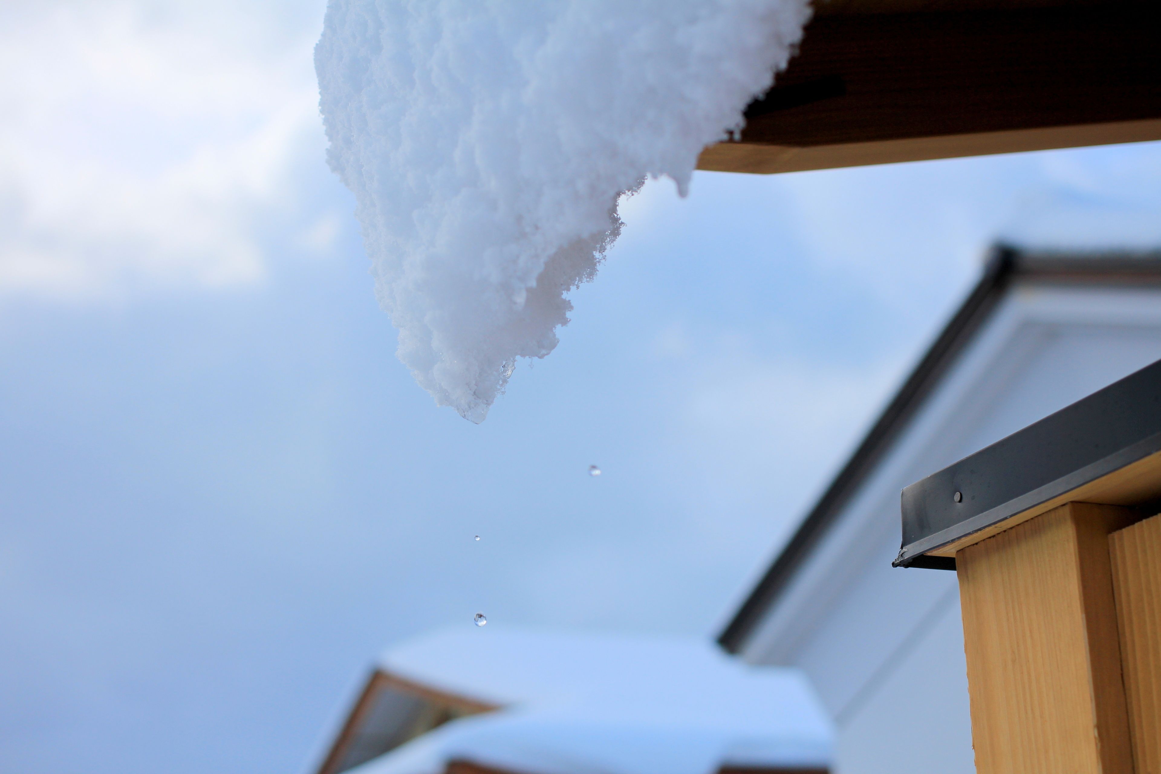Techo cubierto de nieve con una viga de madera y canalón metálico.