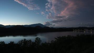 A nighttime view of a lake with mountains in the background and a bridge with lights reflecting on the water.