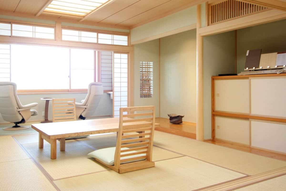 A traditional Japanese room with tatami flooring, a low table, two chairs, and a sliding door.