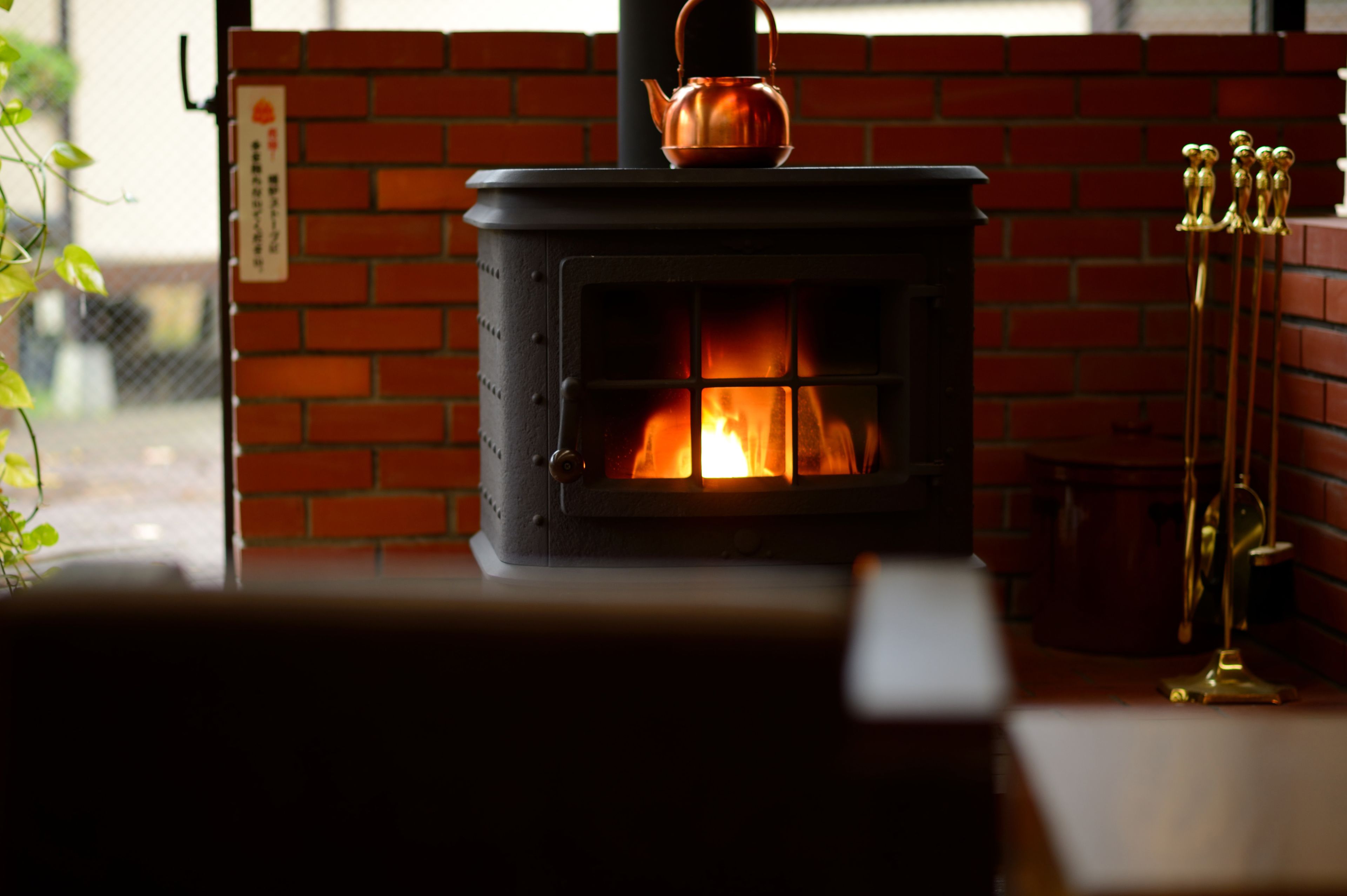 Puuhellassa näkyy avotuli, seinä on tehty tiilistä, ja metallitelineellä on esillä erilaisia esineitä.
