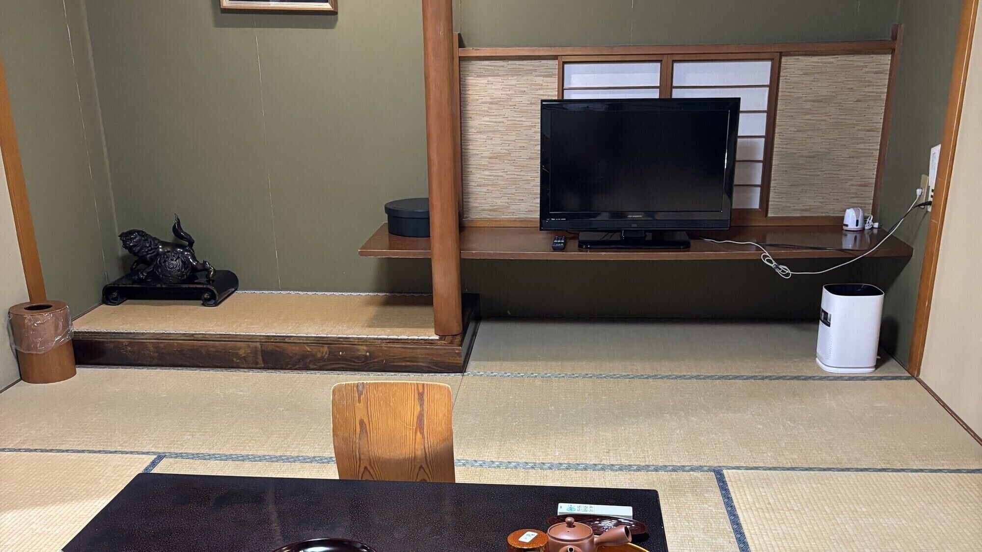 A tatami mat room with a television, a small statue, and a traditional Japanese tea set.
