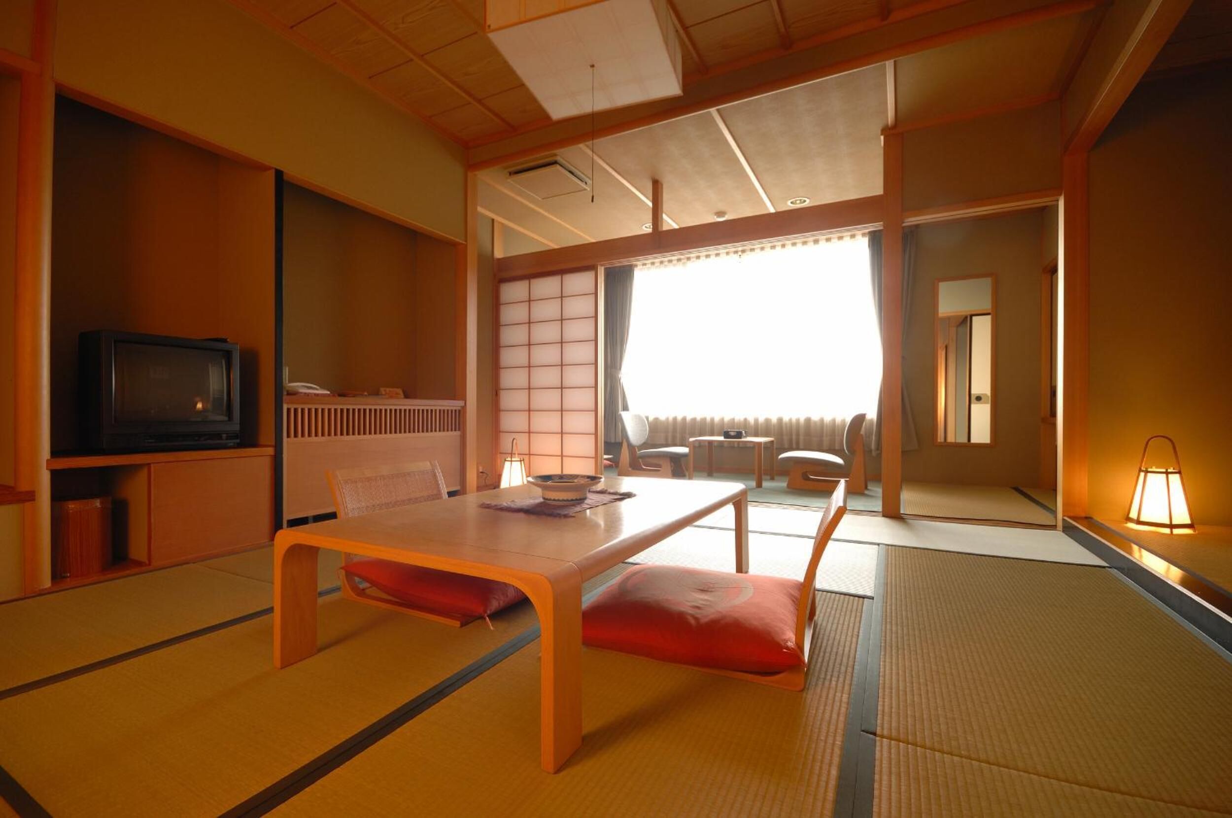 Ein traditioneller japanischer Raum mit Tatami-Böden, einem niedrigen Tisch mit Kissen, einem Fernseher und Schiebetüren.