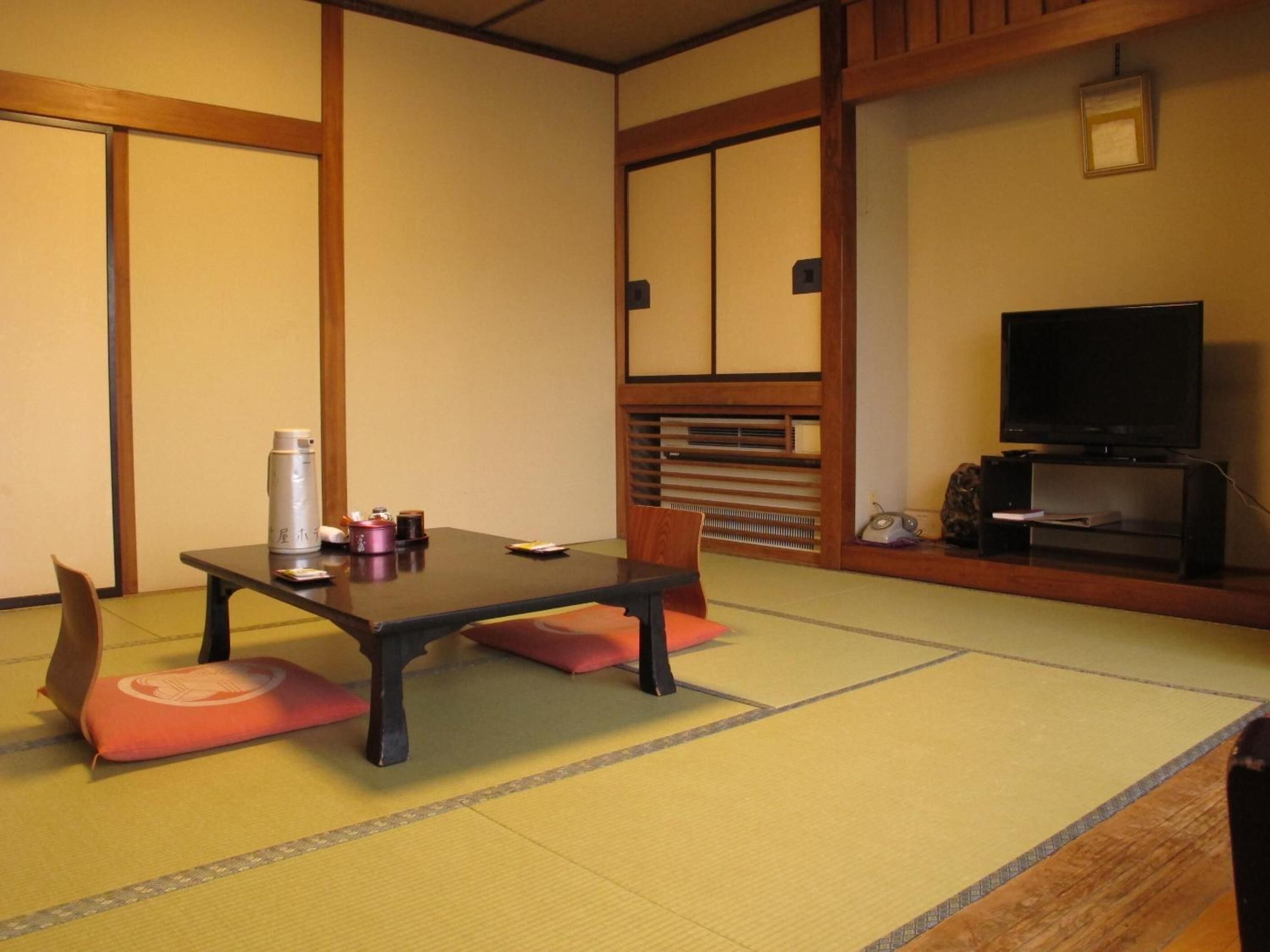 Una habitación japonesa tradicional con suelo de tatami, una mesa baja, un televisor y un armario de madera.