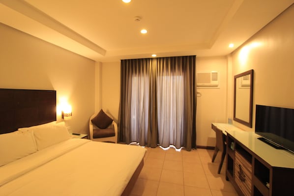 A hotel room with a bed, a desk, a chair, a TV, and curtains. - Lagoon Coron (Coron)