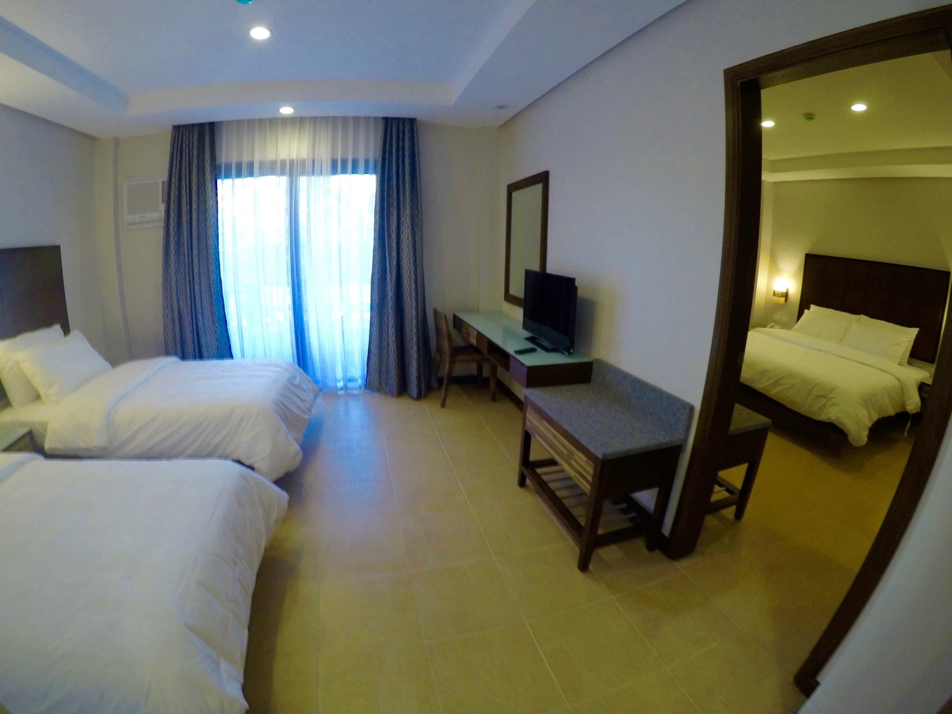 A hotel room with two beds, a desk with a TV, a mirror, and a window with curtains.