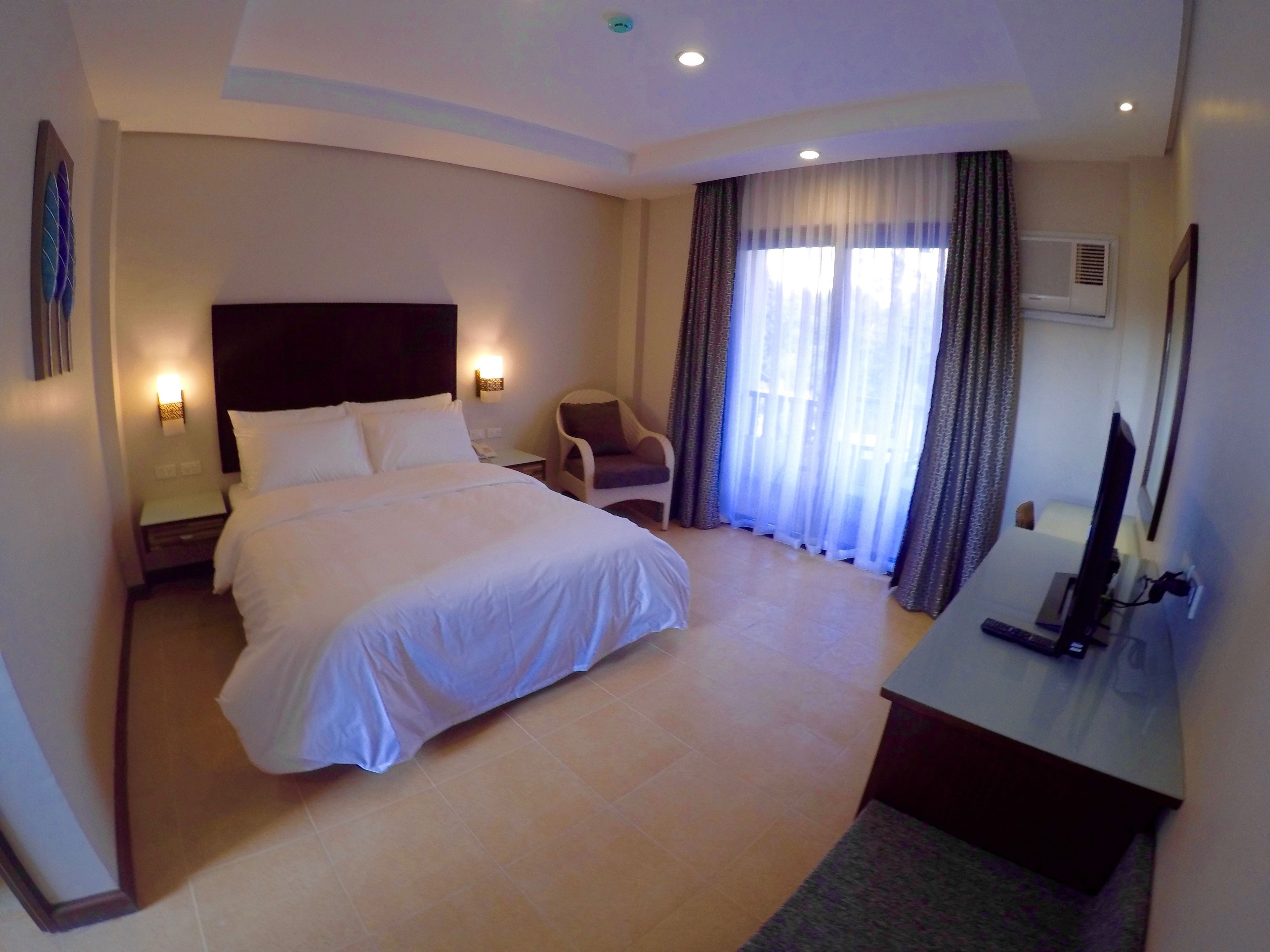 Une chambre d’hôtel avec un grand lit, un bureau avec un ordinateur, une chaise, une télévision et une fenêtre avec des rideaux.