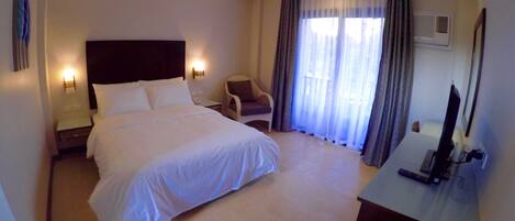 Une chambre d’hôtel avec un grand lit, un bureau avec un ordinateur, une chaise, une télévision et une fenêtre avec des rideaux.