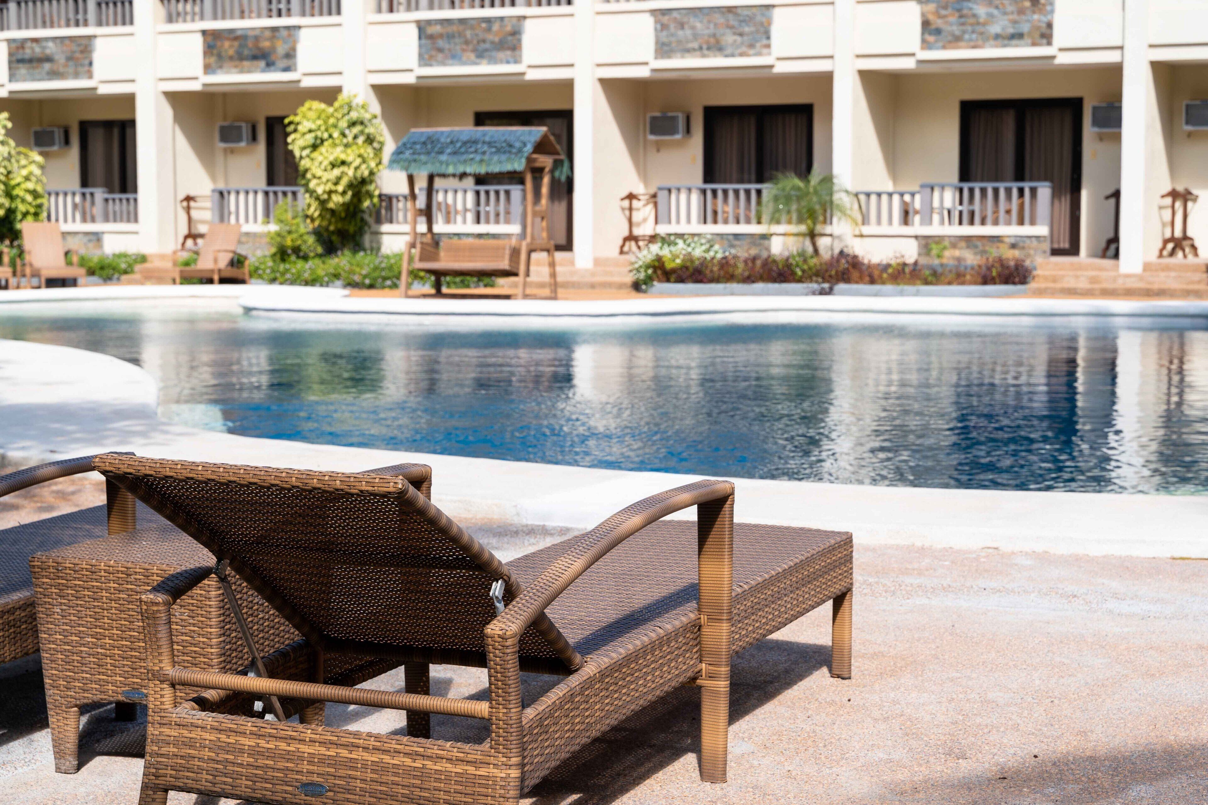A poolside area with wicker lounge chairs and a building with balconies in the background.