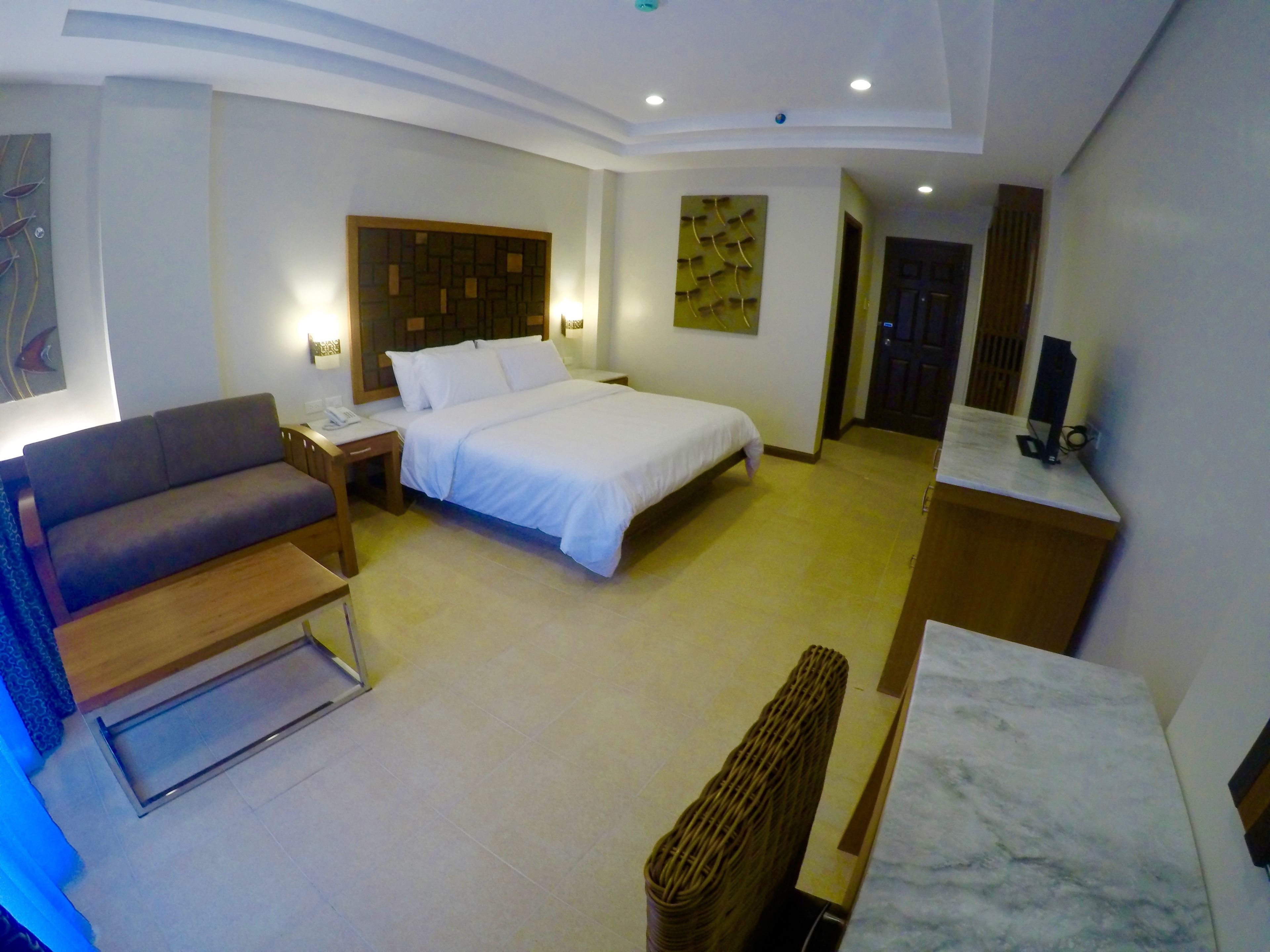 A modern hotel room with a bed, a sofa, a desk, and a TV.