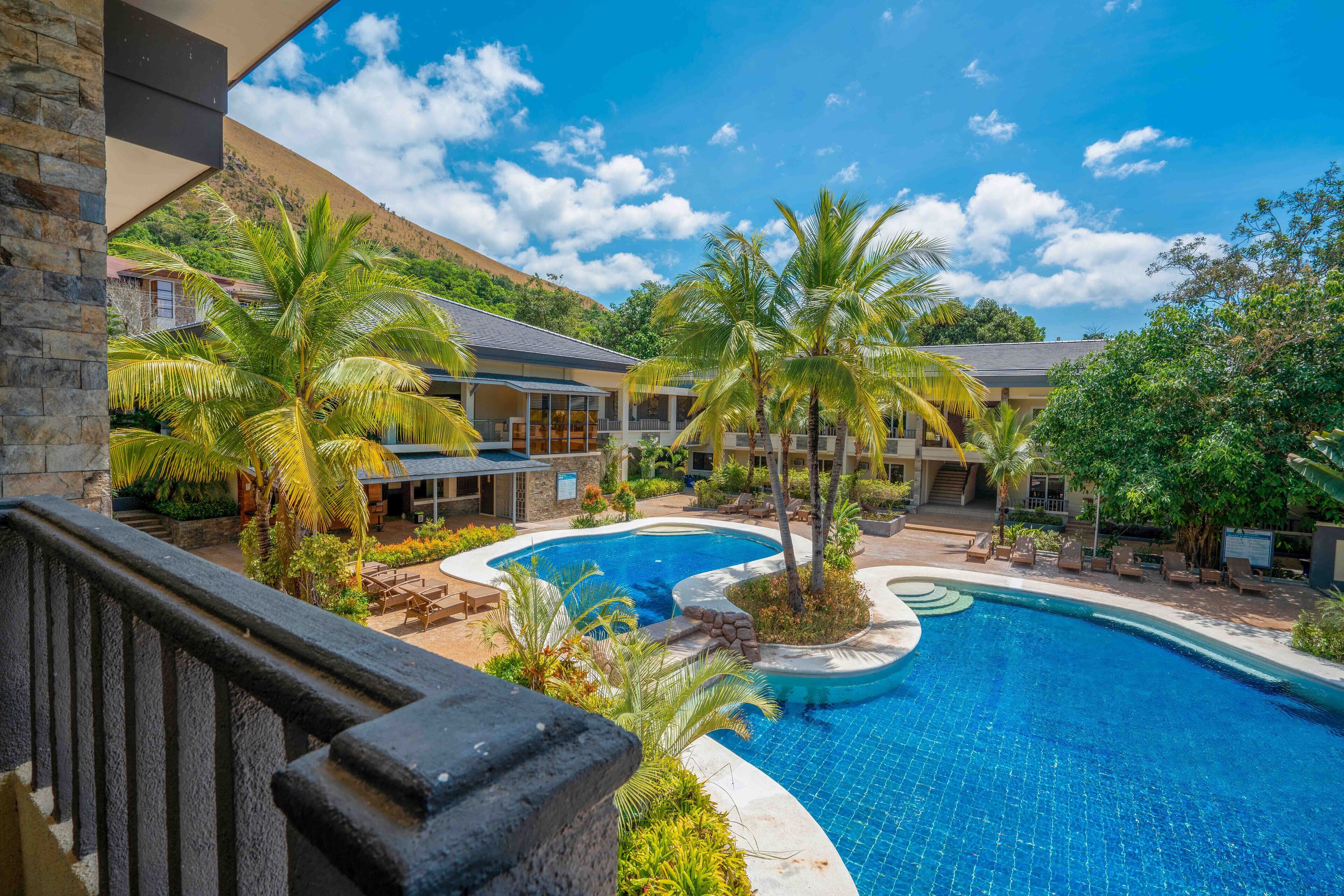 Resort com uma piscina grande, palmeiras e montanhas ao fundo.