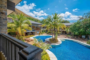 A resort with a large swimming pool, palm trees, and a mountainous backdrop.