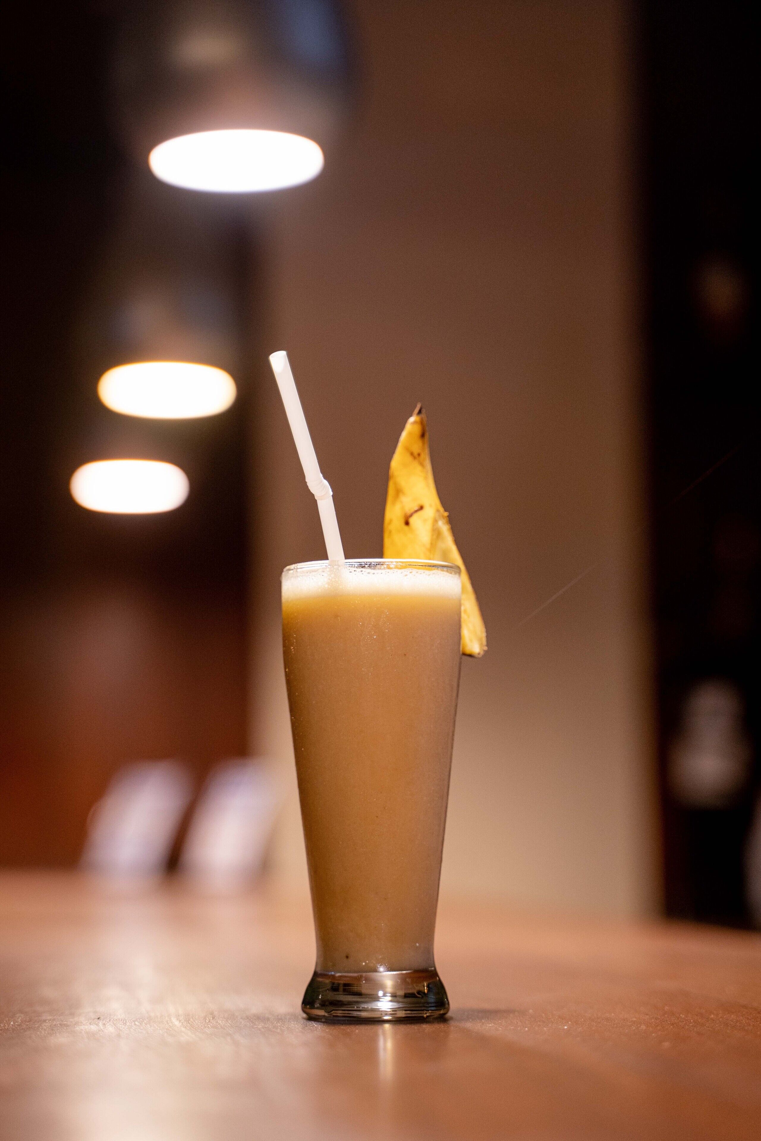 A tall glass with a straw and a slice of pineapple on the rim, placed on a wooden surface.