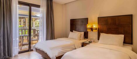 A hotel room with two beds, a balcony with a table and chairs, and a wooden headboard with a lamp.