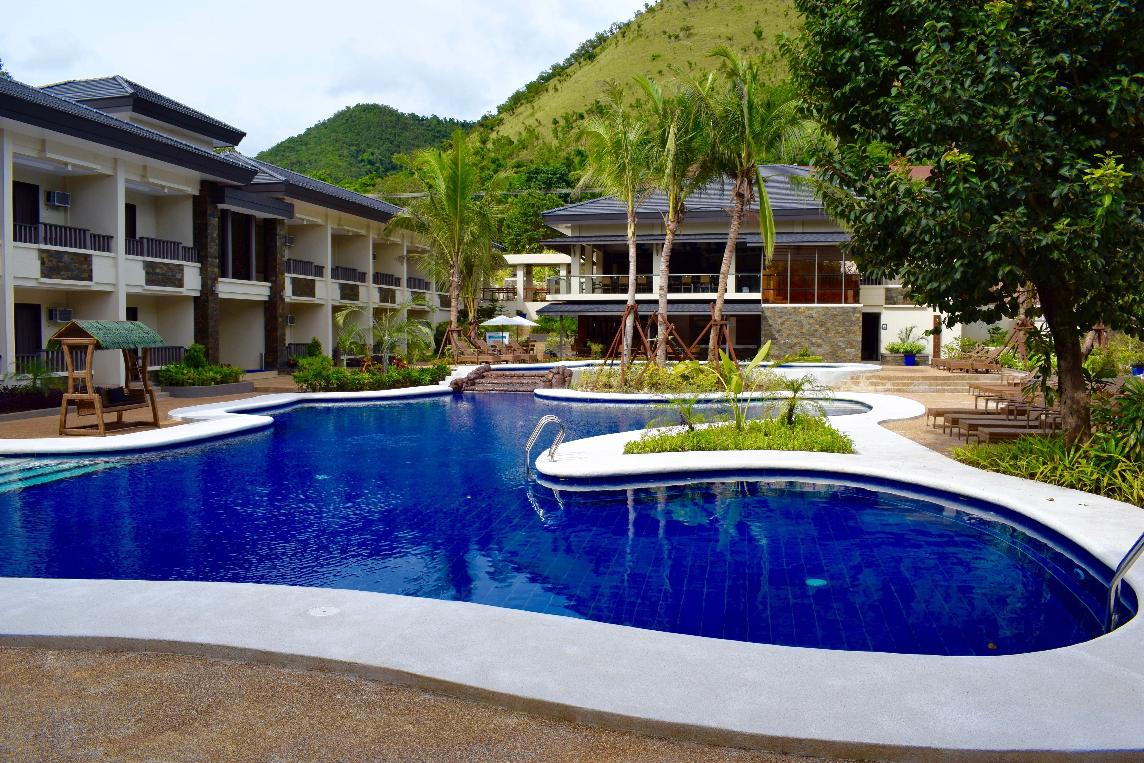 Un hotel con una amplia piscina, varios balcones y abundante vegetación.