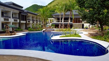 A hotel with a large swimming pool, multiple balconies, and lush greenery.