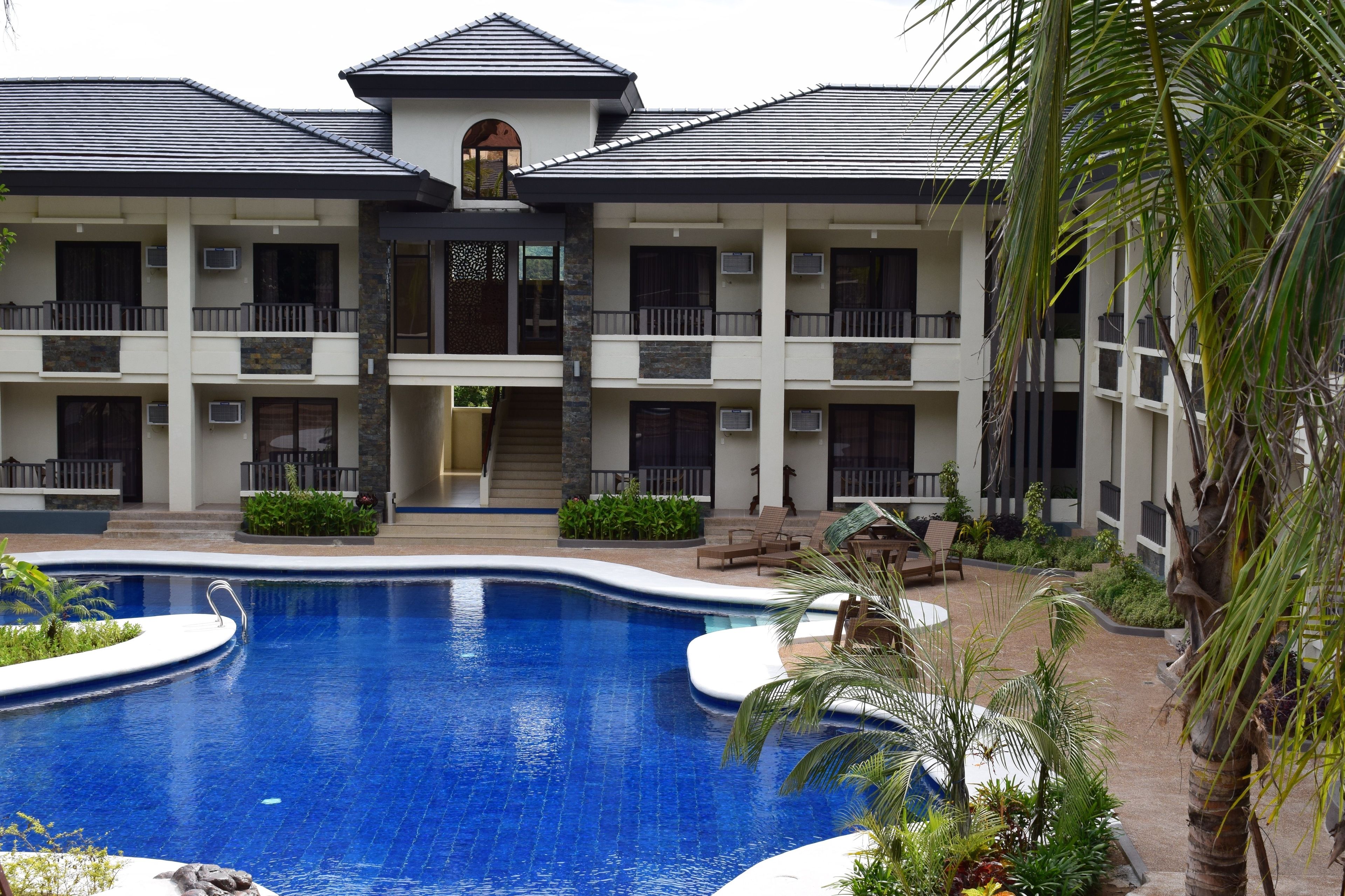 A hotel with a swimming pool, multiple balconies, and a central entrance.