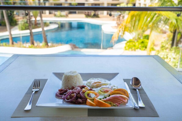 A dining table with a meal consisting of rice, eggs, and various vegetables, set against a view of a swimming pool and palm trees. - Lagoon Coron (Coron)