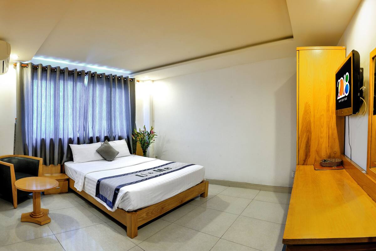 A hotel room with a bed, a wooden nightstand, a TV, and a desk with a chair.