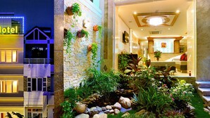A hotel with a sign reading "U & Me Hotel," featuring a modern multi-story building with illuminated windows and a landscaped garden area with rocks and plants. - You And Me Hotel (Ho Chi Minh City)