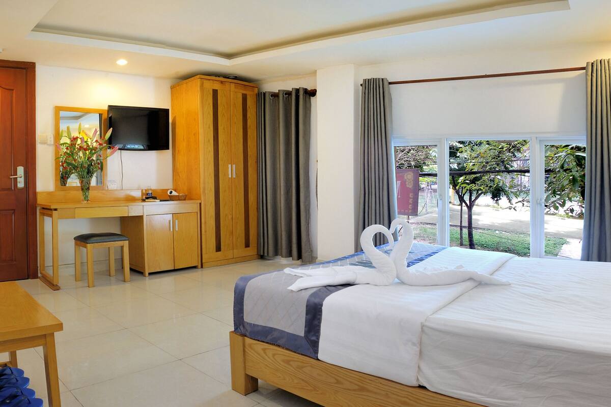 A hotel room with a bed, a desk, a wardrobe, a television, and a view of the outdoors.