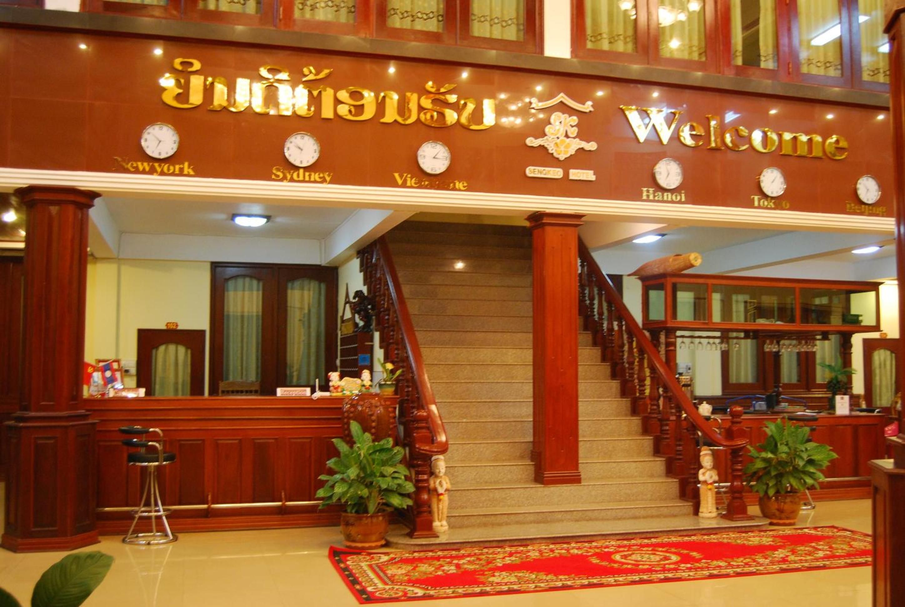 A hotel entrance with a staircase, reception desk, and clocks indicating different cities.