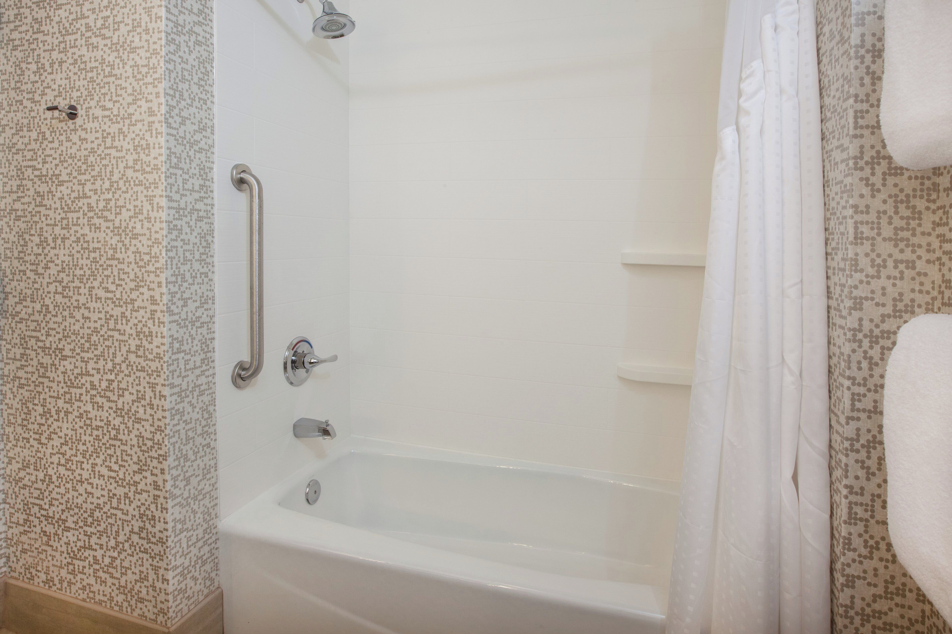 A bathroom with a white bathtub, a shower with a handheld showerhead, and a grab bar.