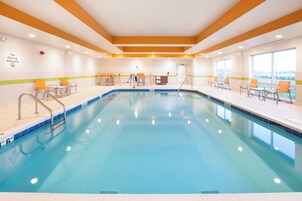 An indoor swimming pool with clear water, surrounded by lounge chairs and a pool lift.