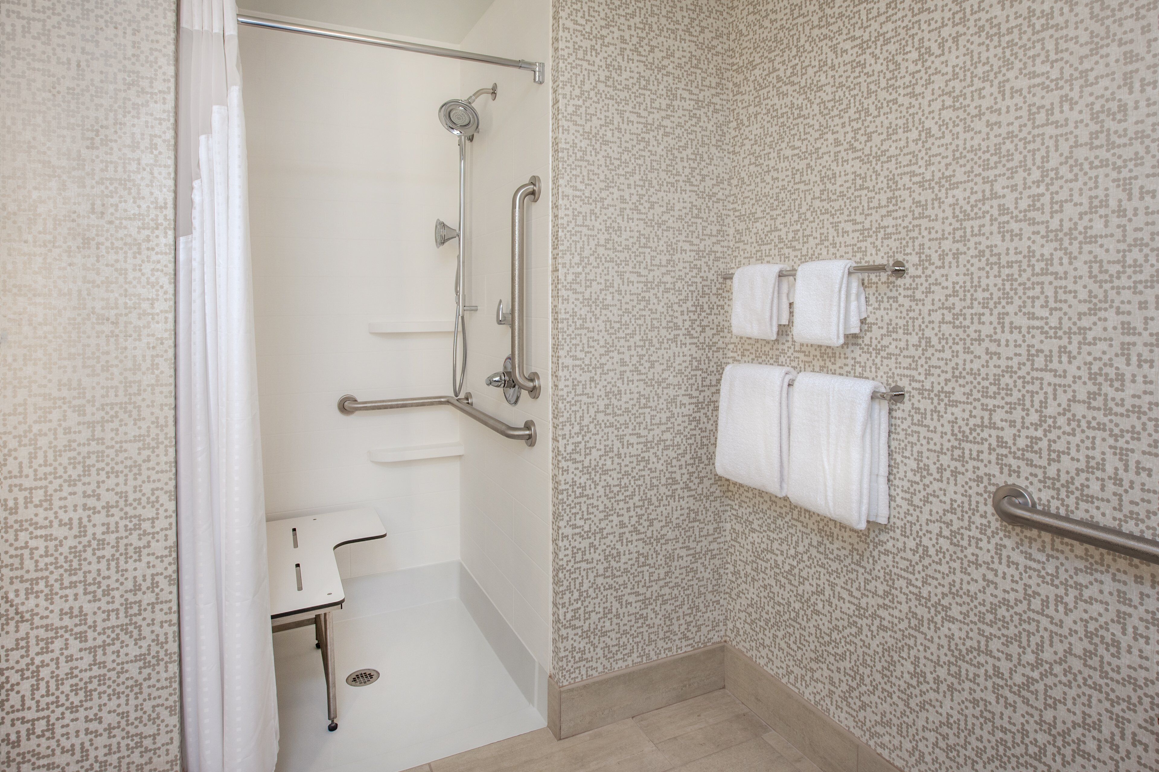A bathroom with a shower, grab bars, a toilet, and a towel rack.