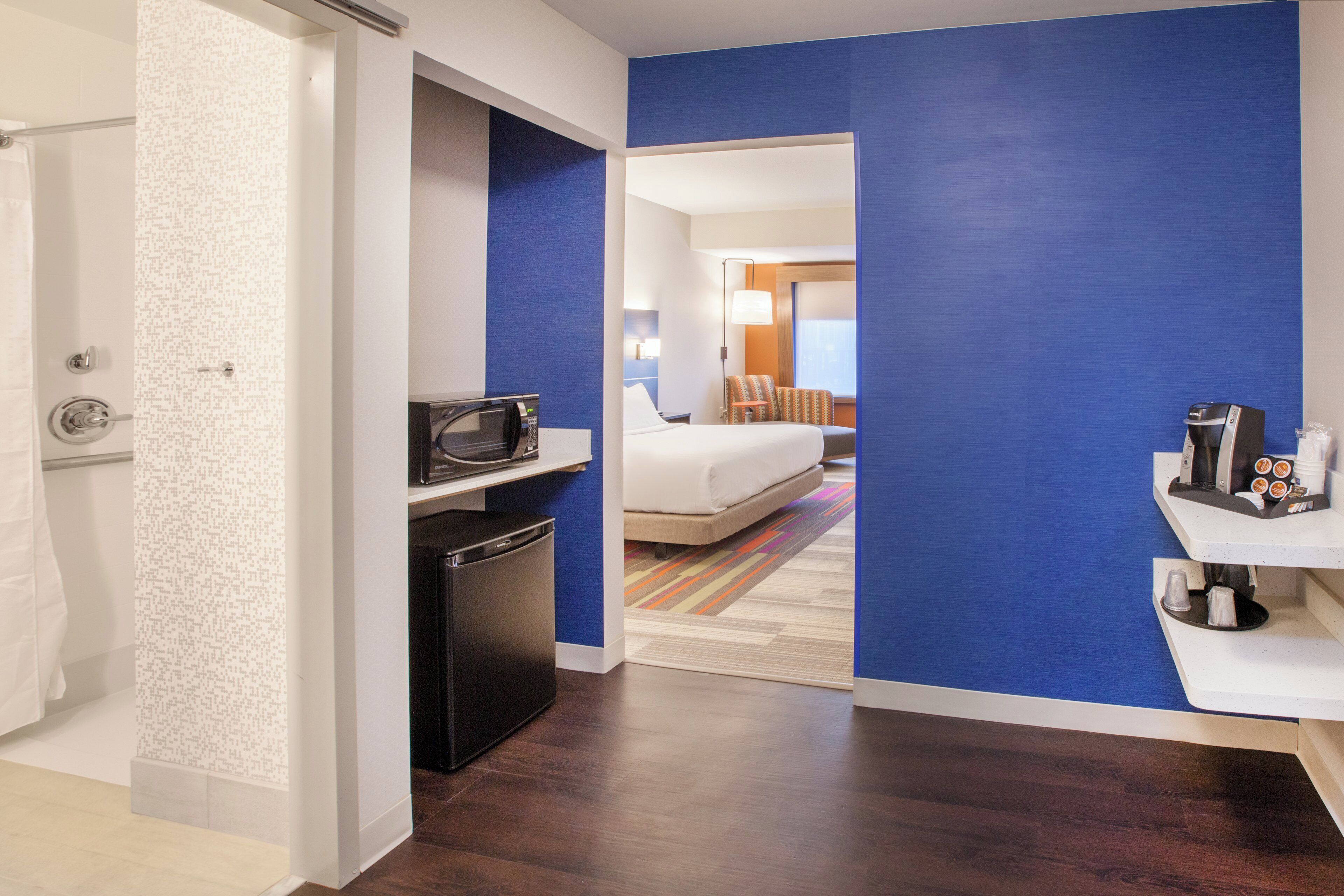 Habitación de hotel con kitchenette, cama, baño y vista al pasillo.
