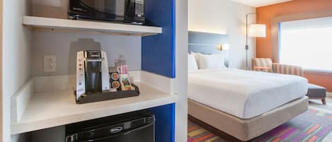 Una habitación de hotel con una cama, microondas, cafetera y refrigerador pequeño.