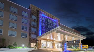 A multi-story hotel with a modern design, featuring a prominent entrance with a covered area and a parking lot in front.