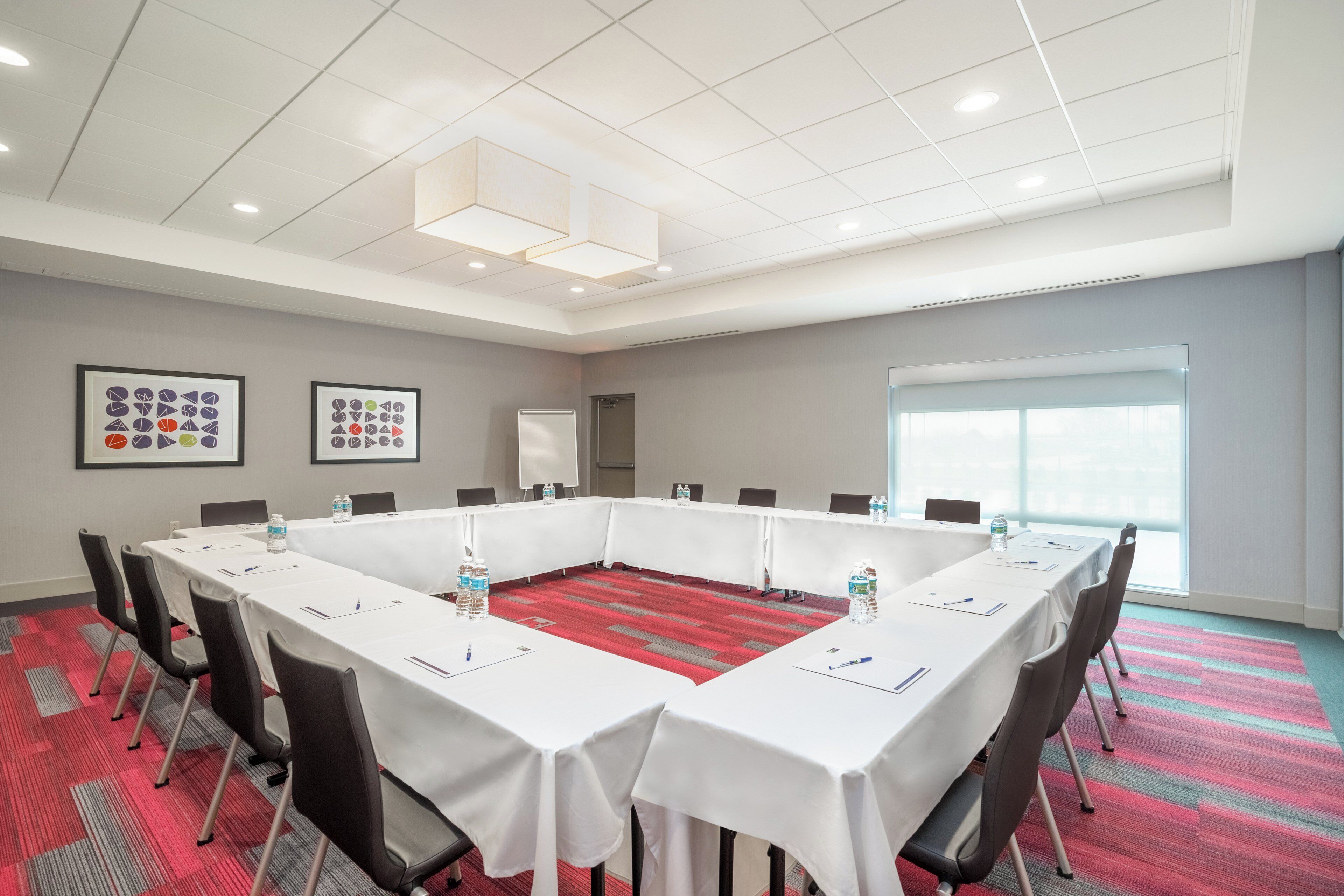 A conference room with a long table, chairs, water bottles, and framed artwork on the wall.