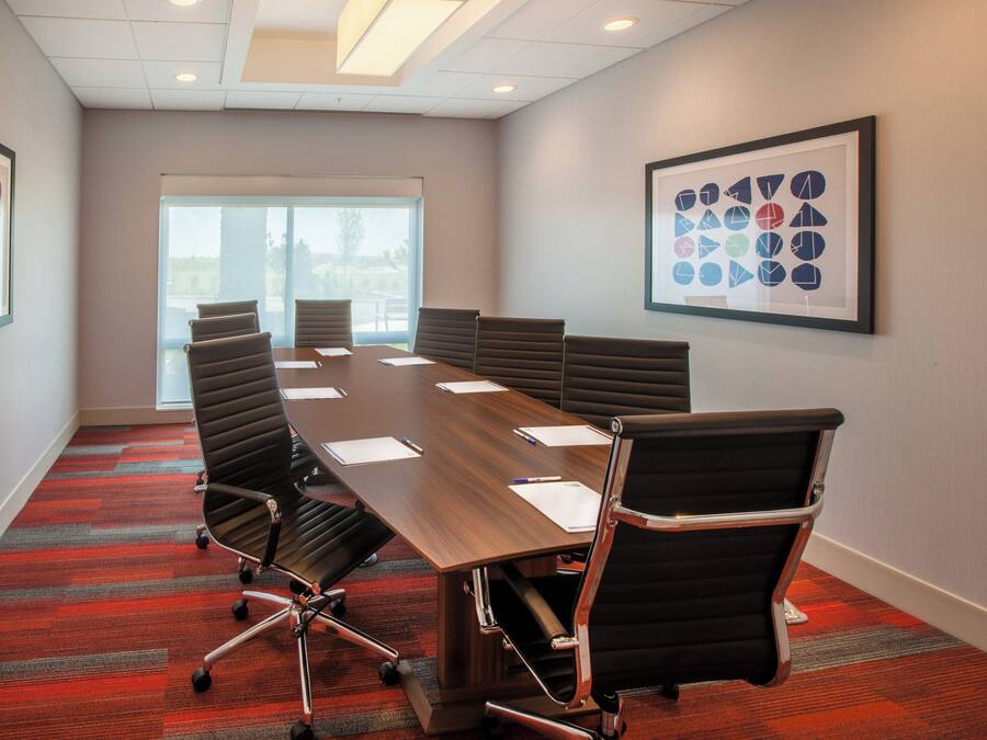 A conference room with a long table, six chairs, and a framed abstract art piece on the wall.
