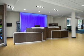 Zona de recepción con pared iluminada en azul, mostrador y área de asientos con sillas y una mesa.