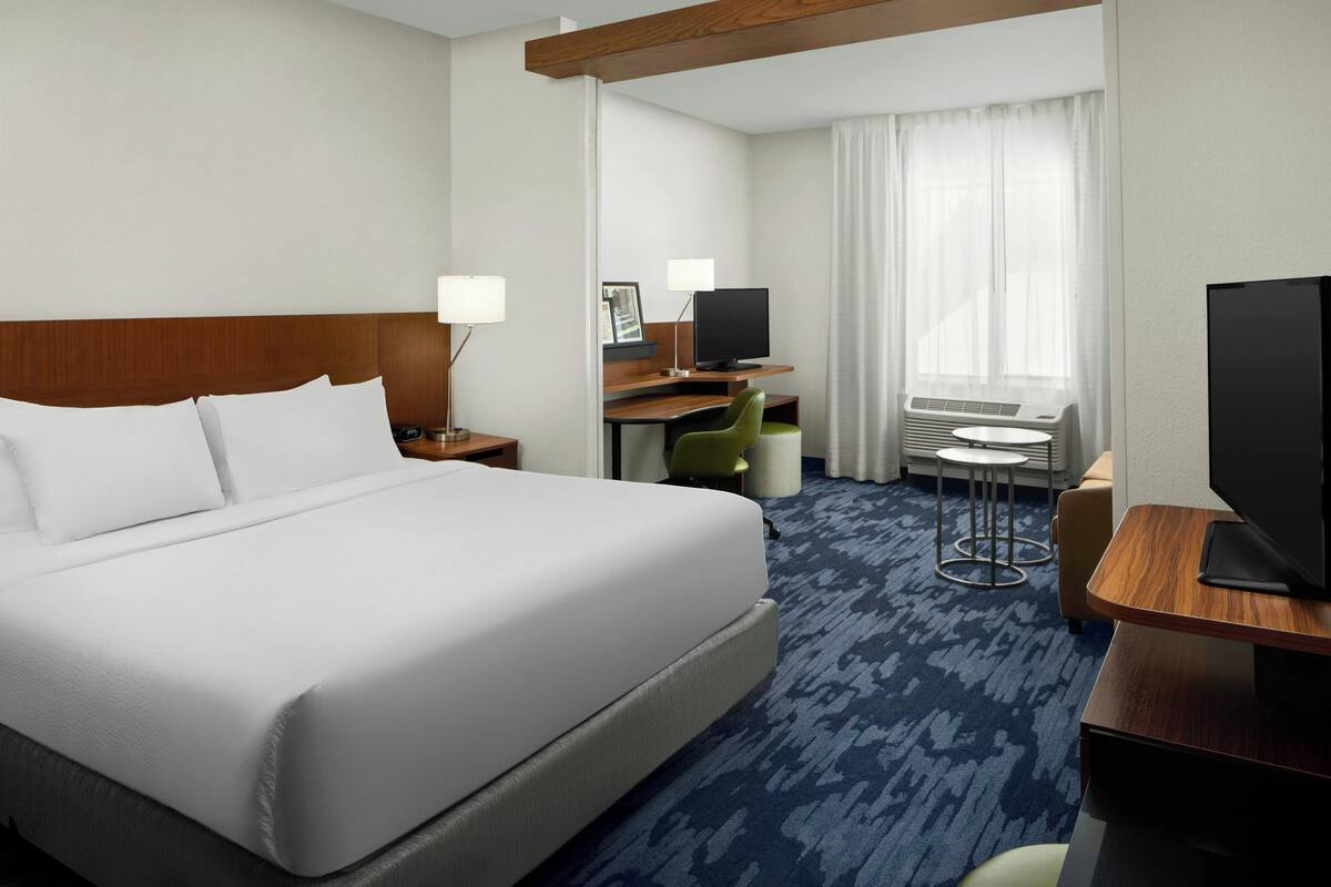 Habitación de hotel con una cama grande, un escritorio con ordenador, televisor y una pequeña zona de estar.