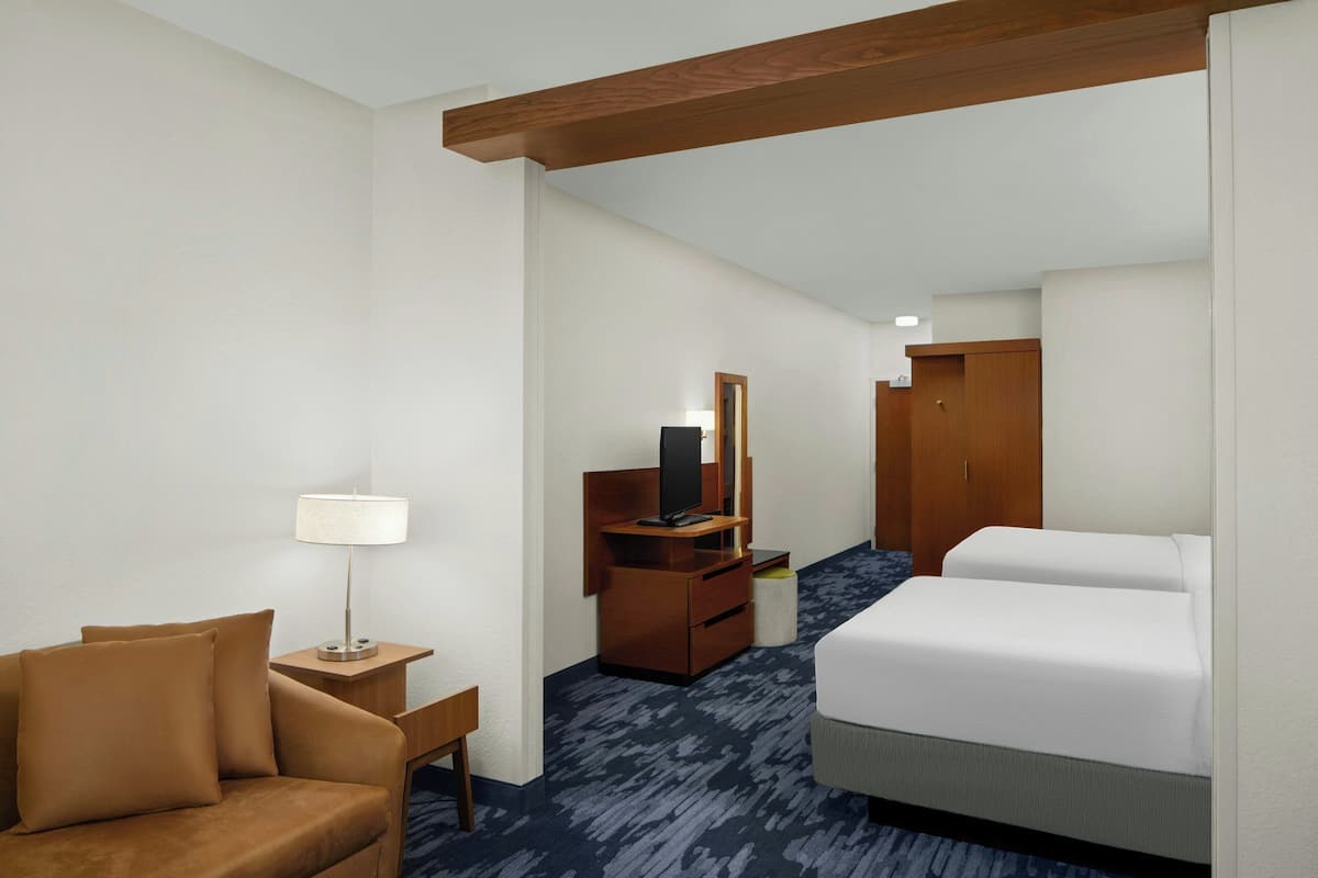 Una habitación de hotel con cama, escritorio con lámpara, televisor y armario.