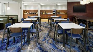 Habitación de hotel con comedor que incluye mesas y sillas, una zona de bar y un televisor montado en la pared.