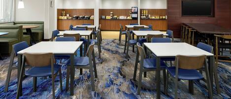 A hotel room with a dining area featuring tables and chairs, a bar area, and a television mounted on the wall.