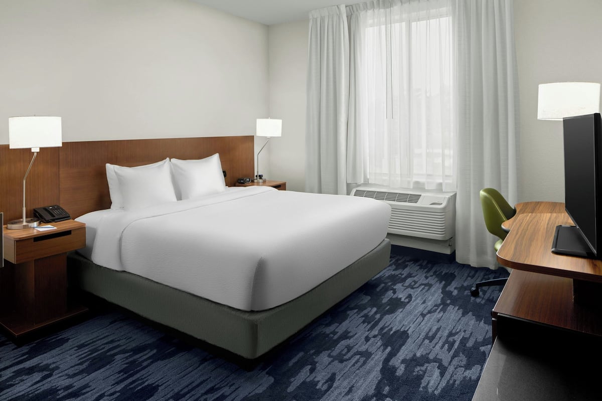 Habitación de hotel con una cama grande, dos mesitas de noche con lámparas, un escritorio con silla y un televisor.