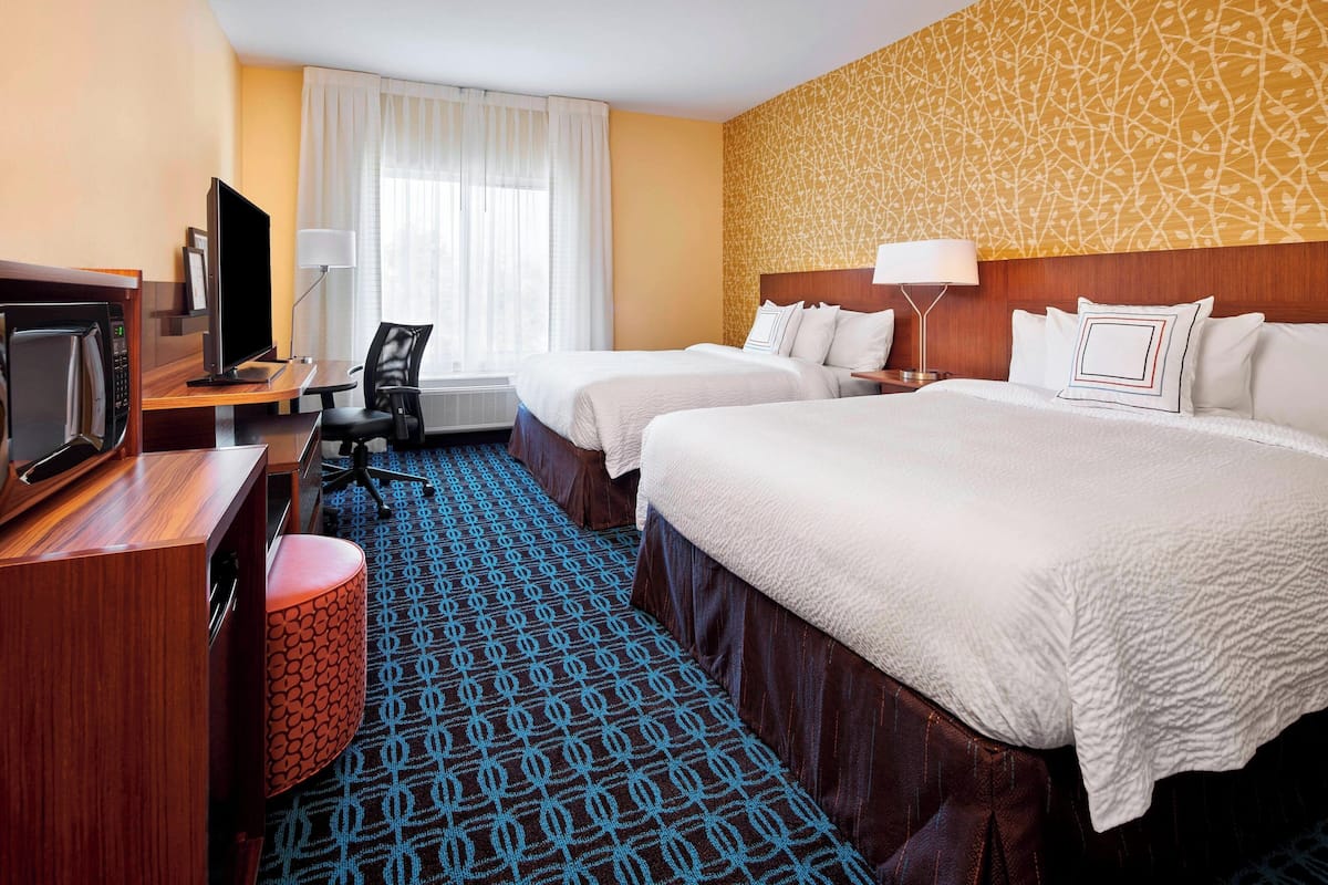 A hotel room with two beds, a desk with a computer, a TV, and a patterned carpet.