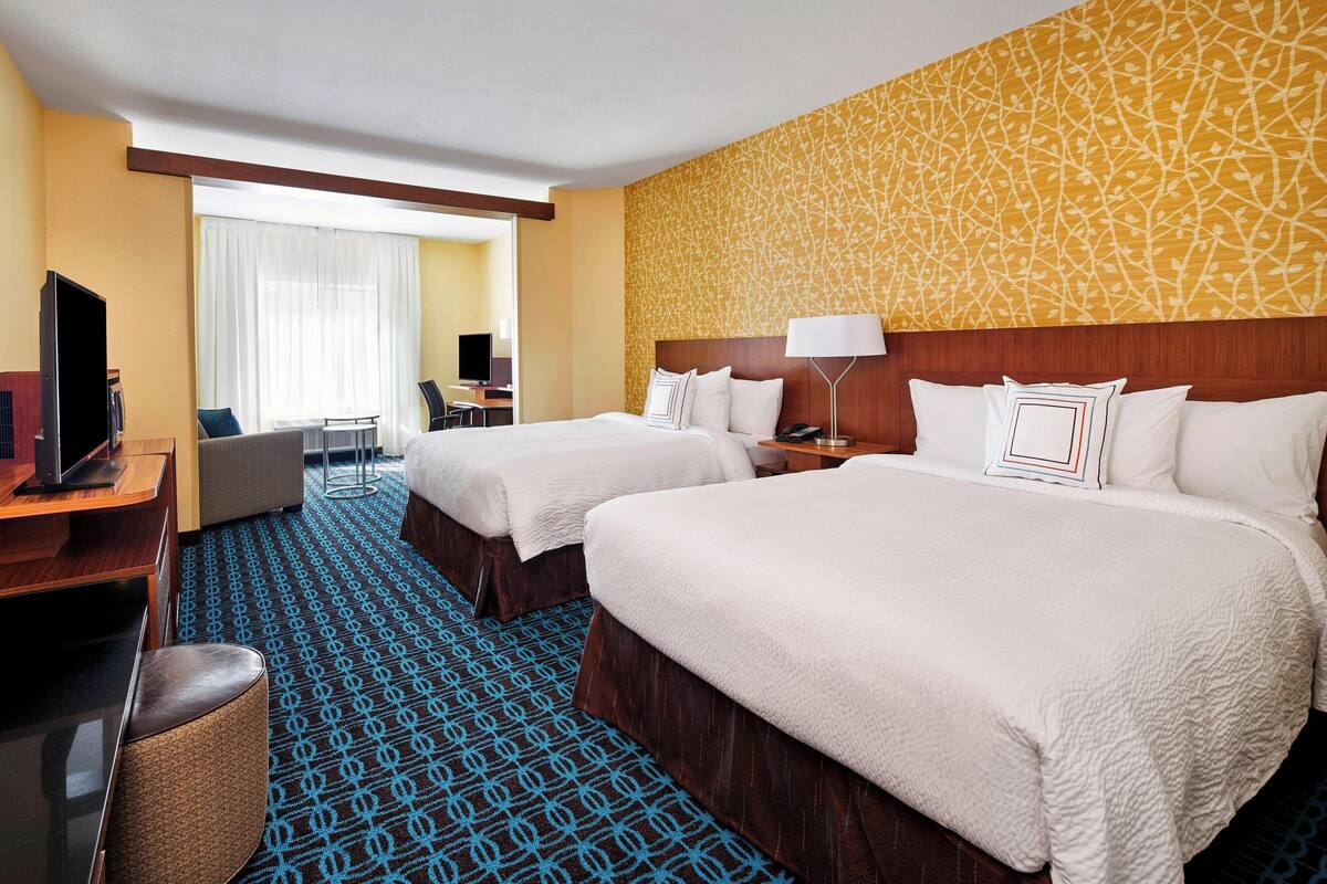 A hotel room with two beds, a desk with a computer, a TV, and a chair.