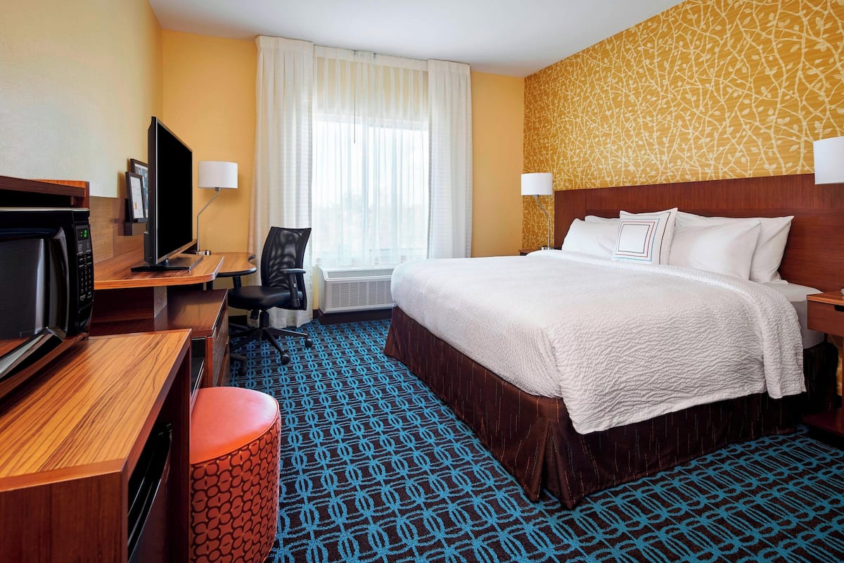 A hotel room with a bed, a desk with a computer, a television, and a chair.