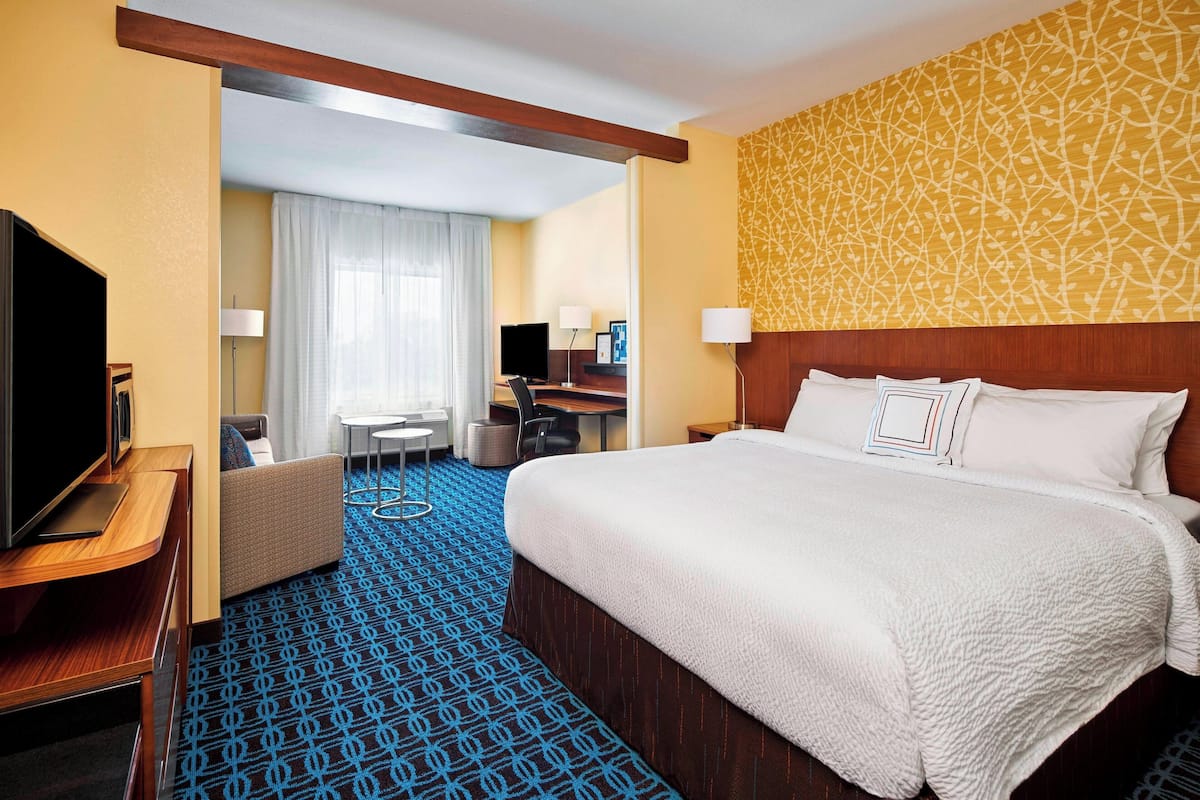A hotel room with a large bed, a desk with a computer, a TV, and a seating area with a sofa and chairs.