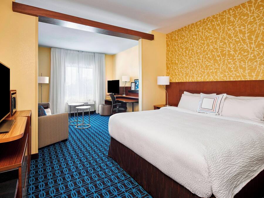 Une chambre d’hôtel dotée d’un grand lit, d’un bureau avec un ordinateur, d’une télévision et d’un coin salon comprenant un canapé et des fauteuils.