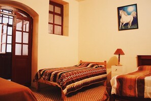 A room with a bed, a nightstand, a lamp, a door, and a window. - Quito Backpacker Guest House (Quito)