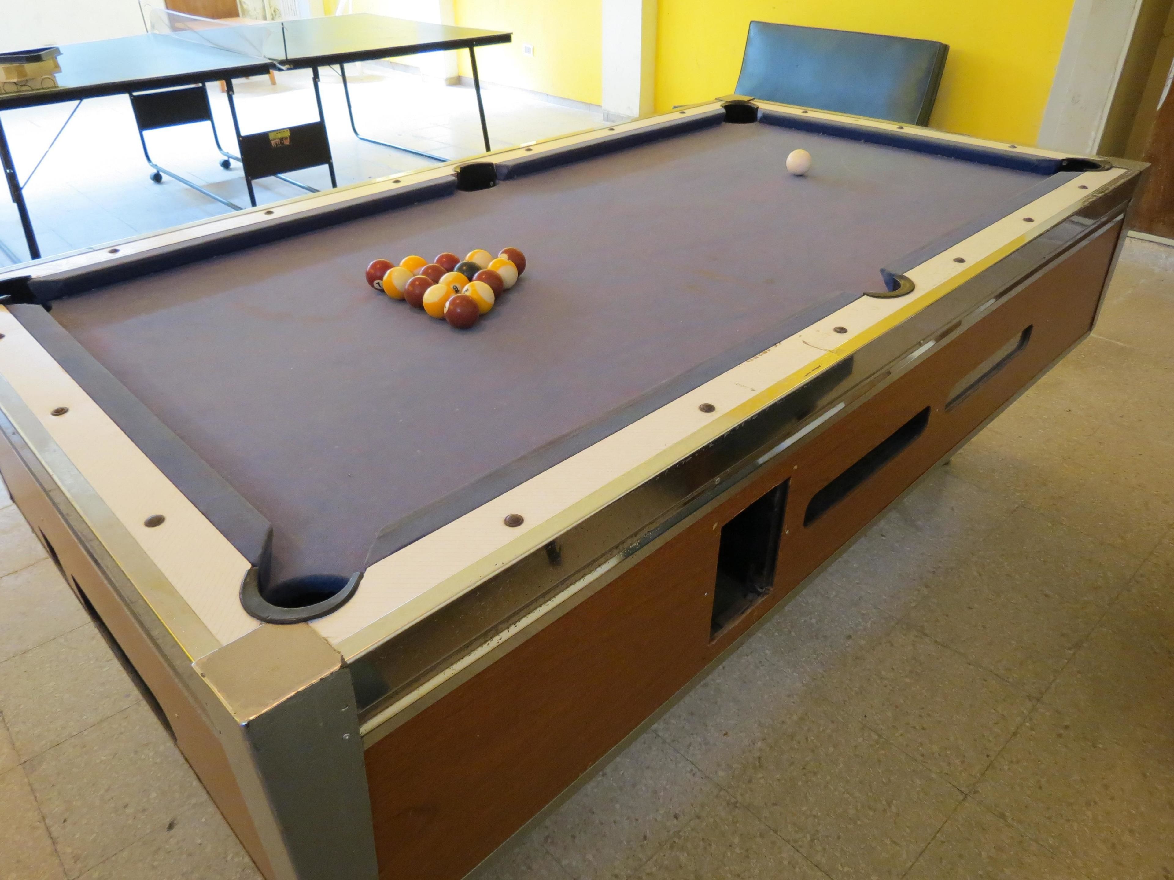 A pool table with balls arranged in a triangle, a table tennis table, and a blue cushioned chair.