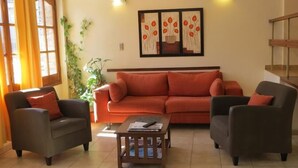 A living room with a sofa, two armchairs, a coffee table, and a painting on the wall. - Hotel Arenales (Villa Carlos Paz)