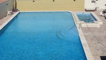 Una piscina rectangular con superficie de agua azul cristalina, rodeada por un suelo de piedra y un muro de ladrillo bajo.